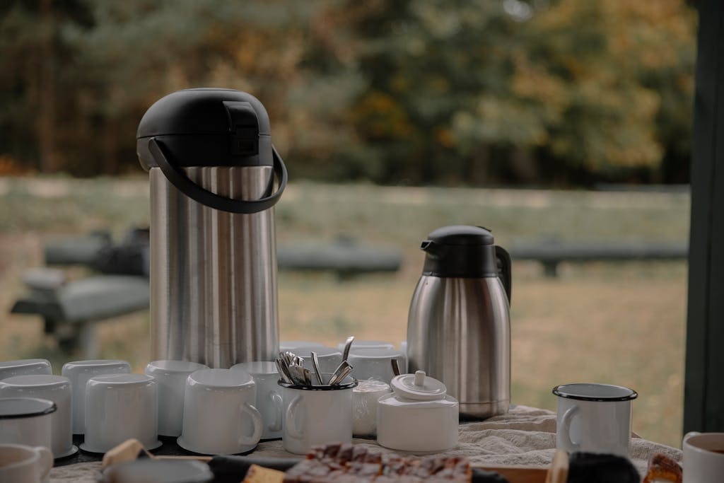 A cozy outdoor coffee setup with thermos, cups, and snacks on a table, perfect for group gatherings.