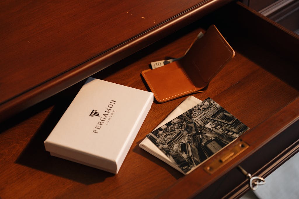 Elegant arrangement of luxury items in a wooden desk drawer, featuring a gift box and wallet.