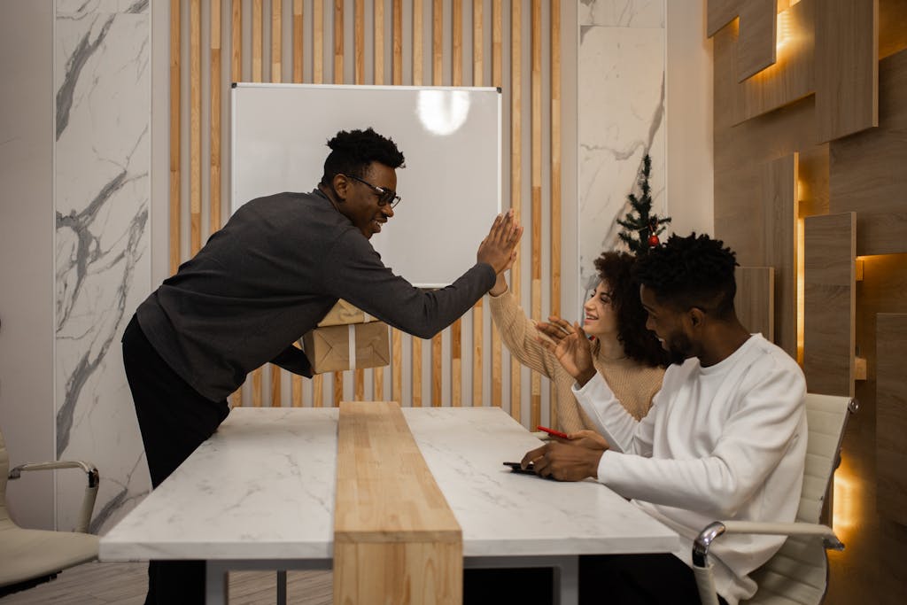 Colleagues celebrate with a high five and gift exchange in a modern office setting.