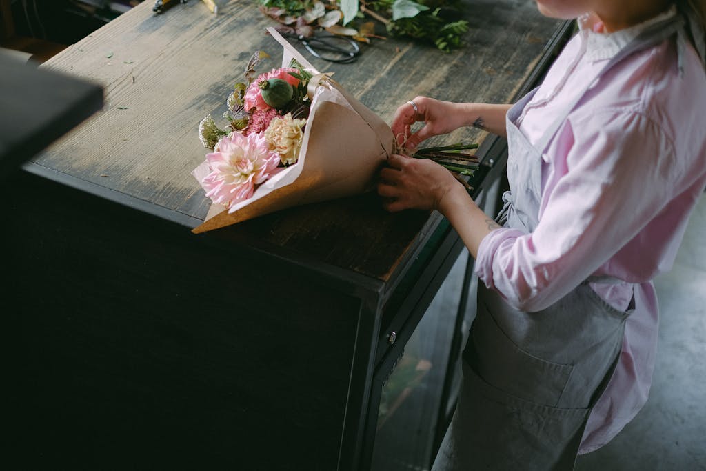 A florist arranges a colorful flower bouquet on a wooden table in a serene indoor setting.