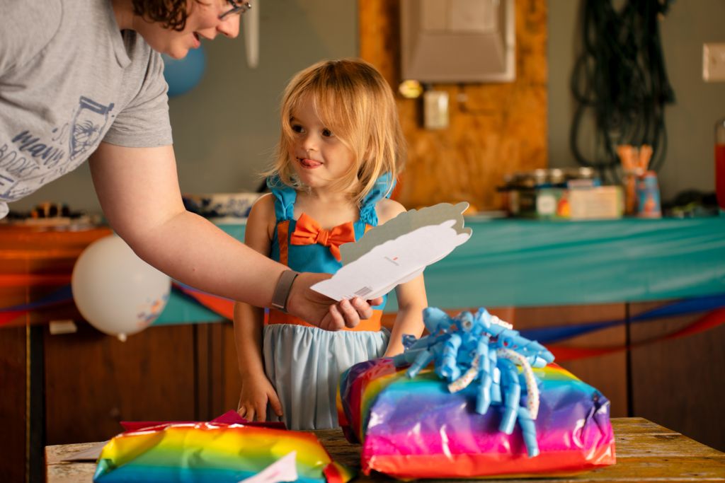 Charming moment of a young girl excitedly opening colorful birthday presents indoors.