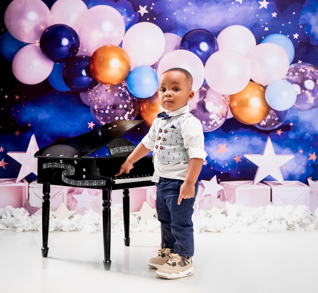 A young boy at a birthday party with a toy piano in a vibrant balloon setting.
