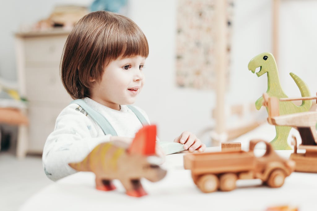 A happy child playing with wooden dinosaur toys in a bright playroom setting.