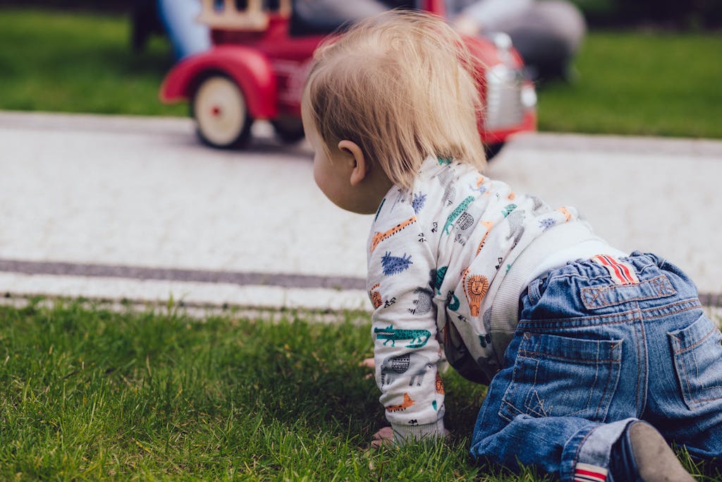 A toddler crawling on green grass outdoors near a toy car, enjoying a sunny day.