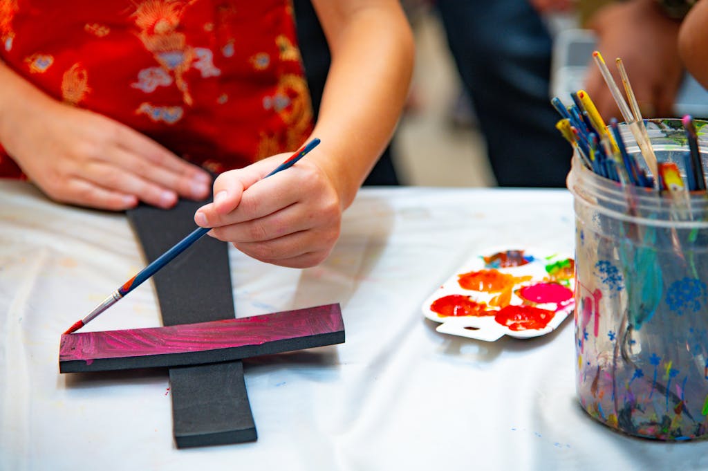 Child painting a small craft with vibrant watercolors on a table indoors.