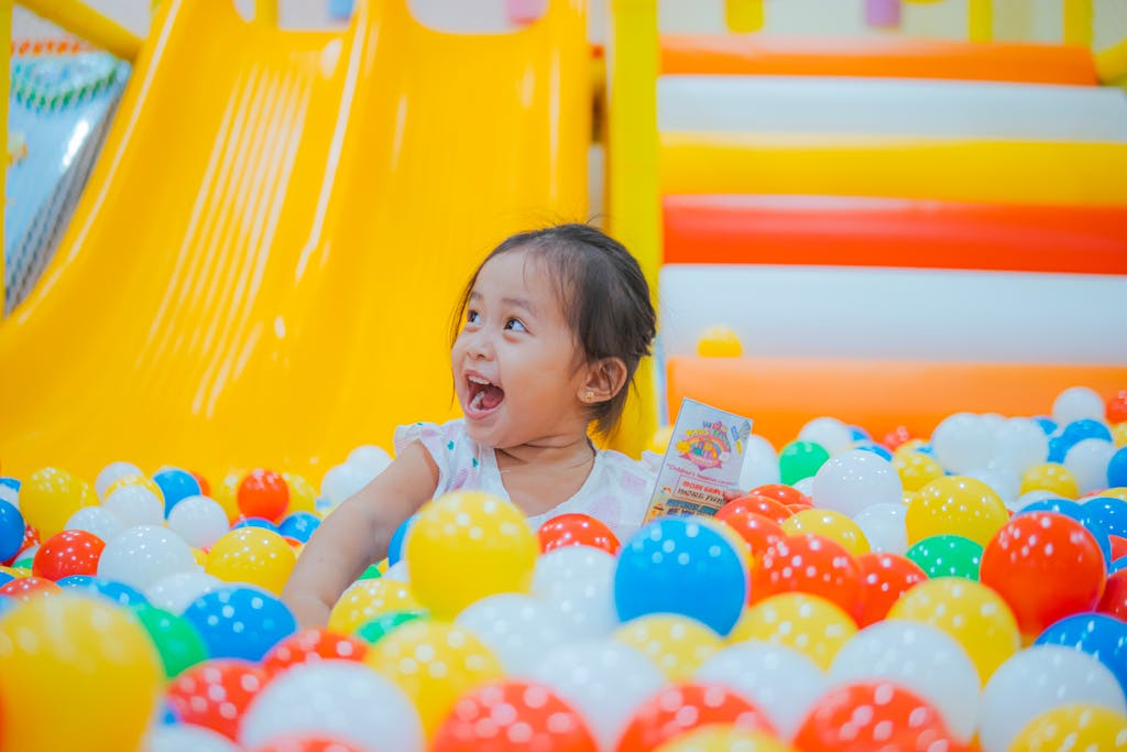 A happy child laughing and playing in a vibrant multicolor ball pit indoor play area.