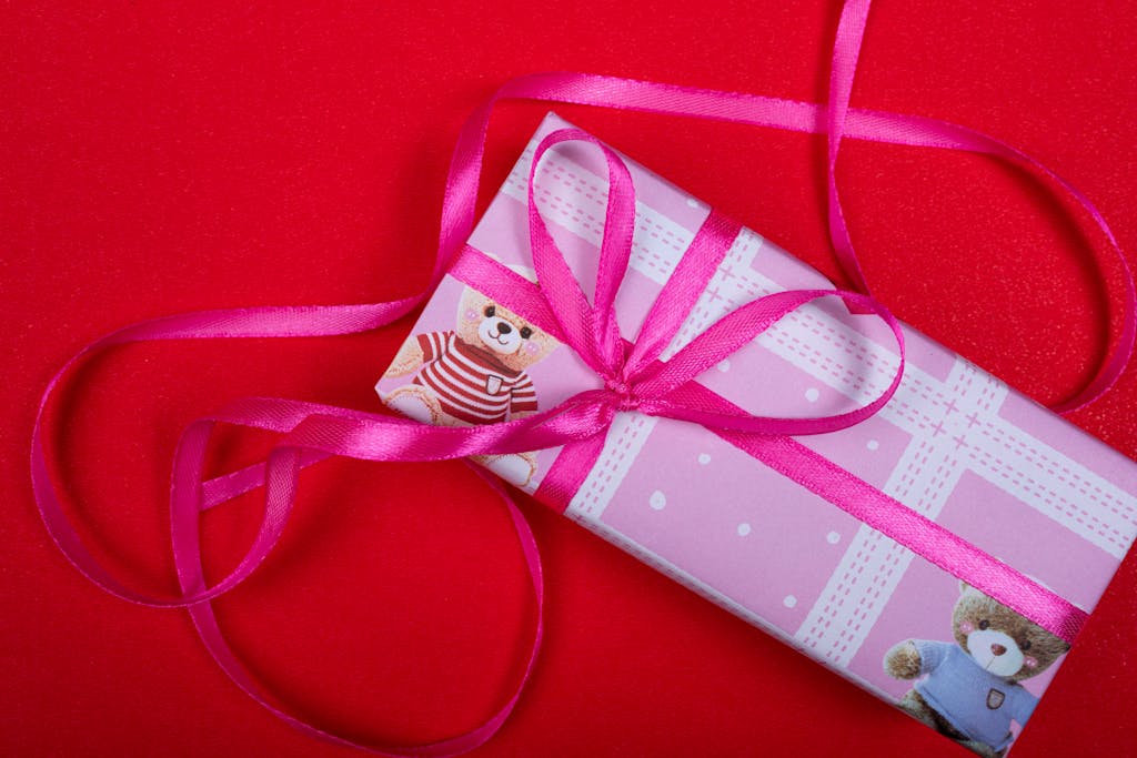 Overhead view of a pink gift box tied with ribbon on a vibrant red background.