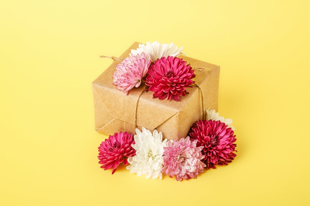Charming gift box adorned with red and white chrysanthemums on a bright yellow backdrop, perfect for celebrations.