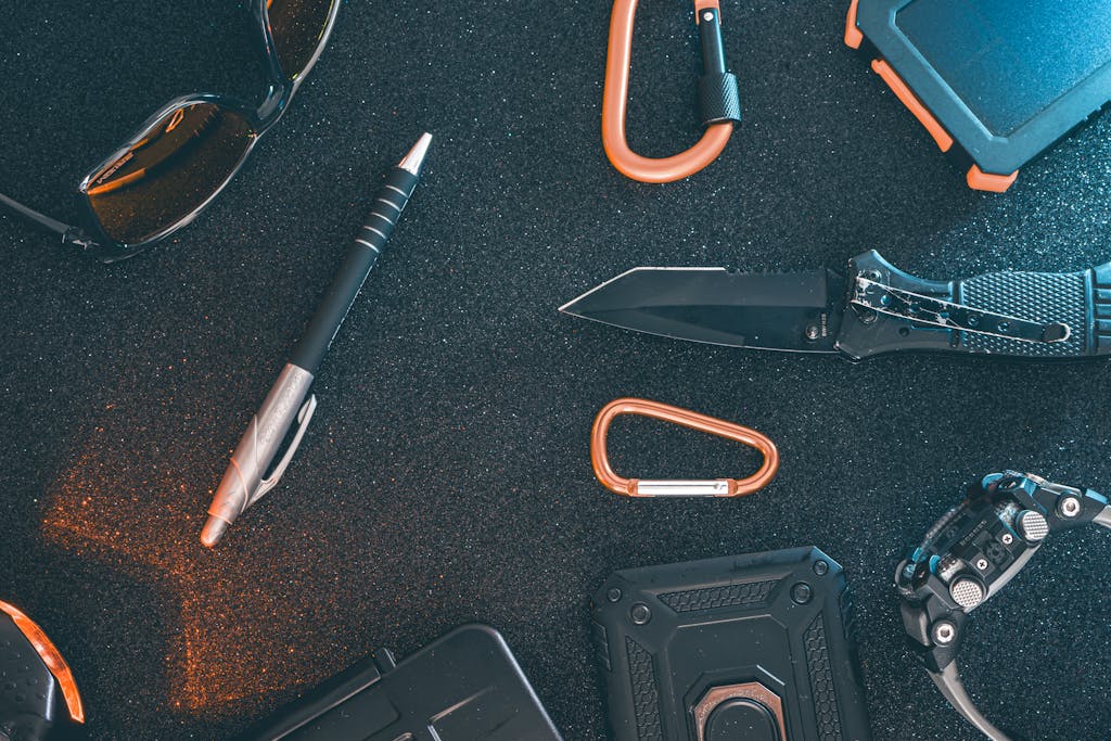 Flat lay of essential EDC gear featuring a pen, knife, sunglasses, and more on a textured background.