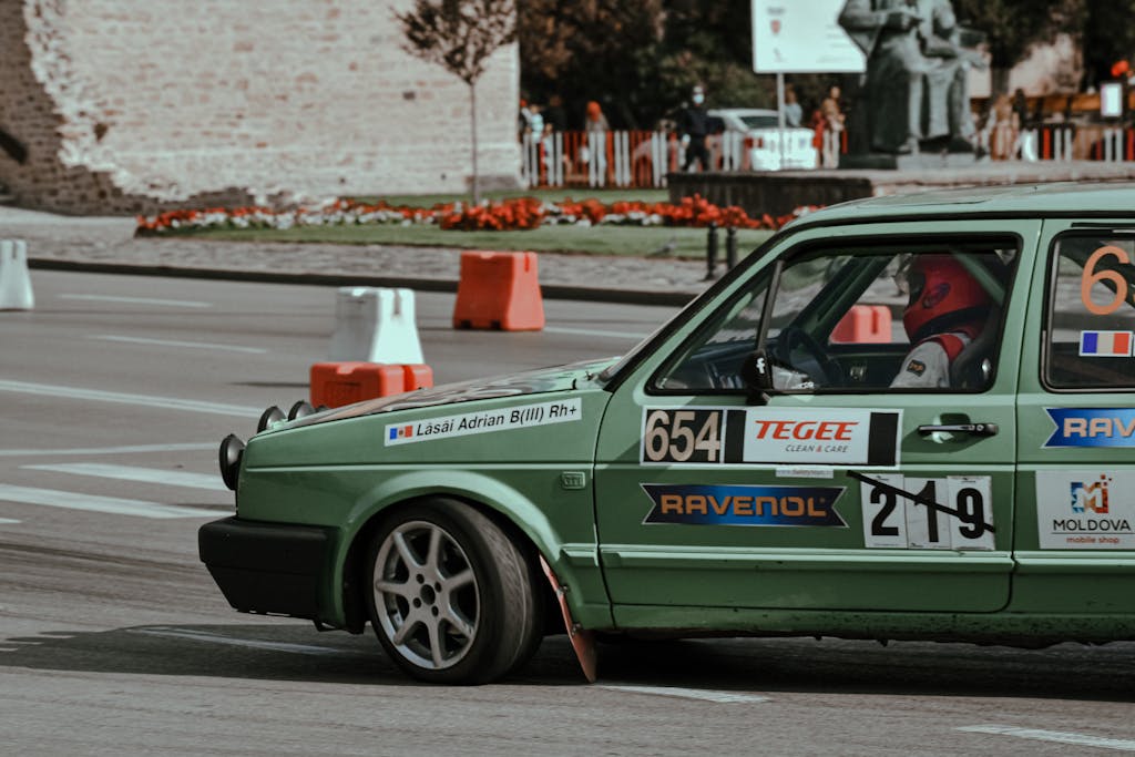 Green car with stickers driving on asphalt city street while participating in rally