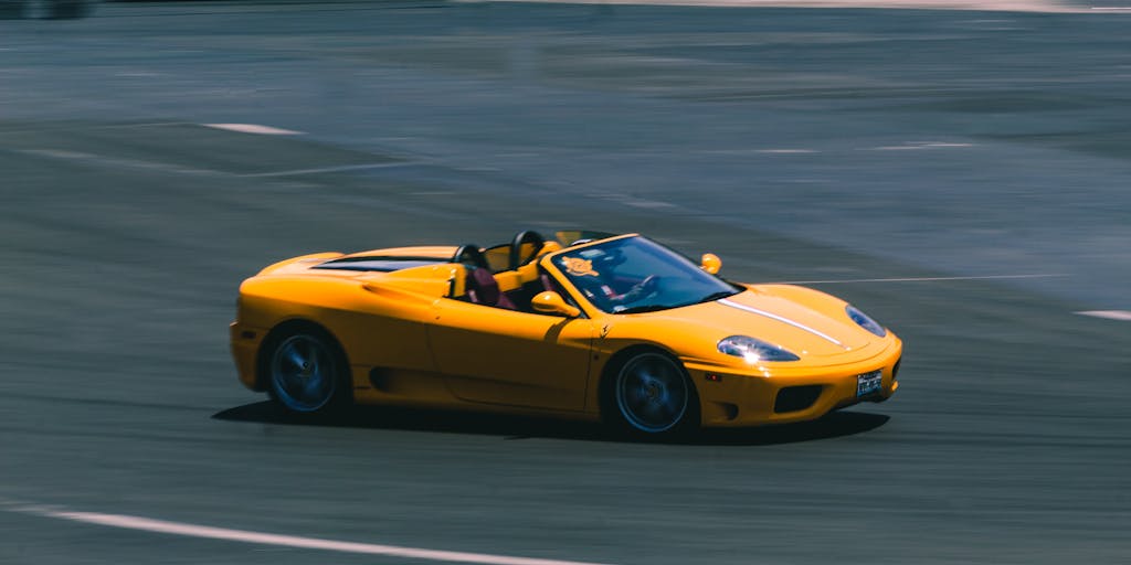 A vibrant yellow convertible sports car speeding on a racetrack, showcasing blurred motion and high speed.