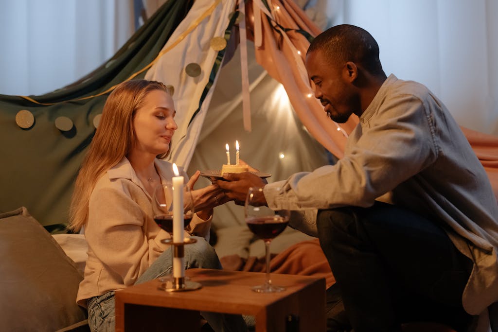 A couple celebrating a birthday indoors with candles and wine, creating a romantic atmosphere.