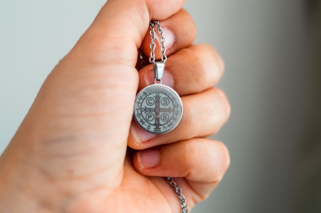 A hand holding a silver Saint Benedict Medal, symbolizing protection and faith.