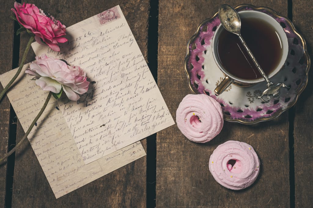 Vintage style tea scene with pink flowers, handwritten letters, and porcelain cup for an aesthetic vibe.
