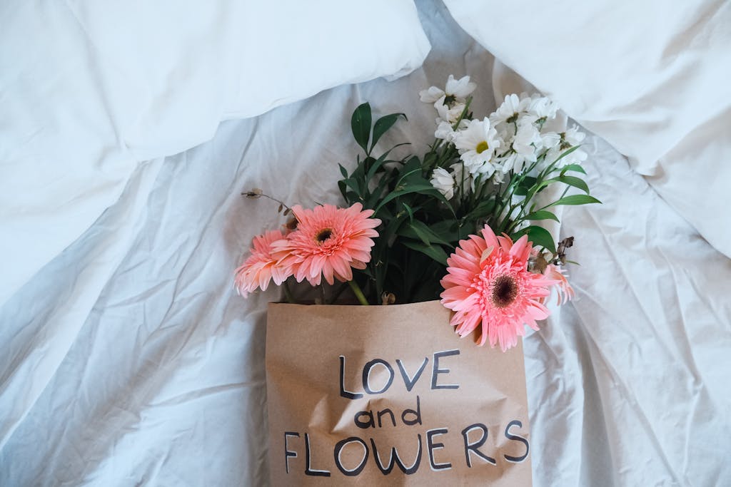A bouquet of flowers with a love message rests on cozy white bedsheets, symbolizing romance.