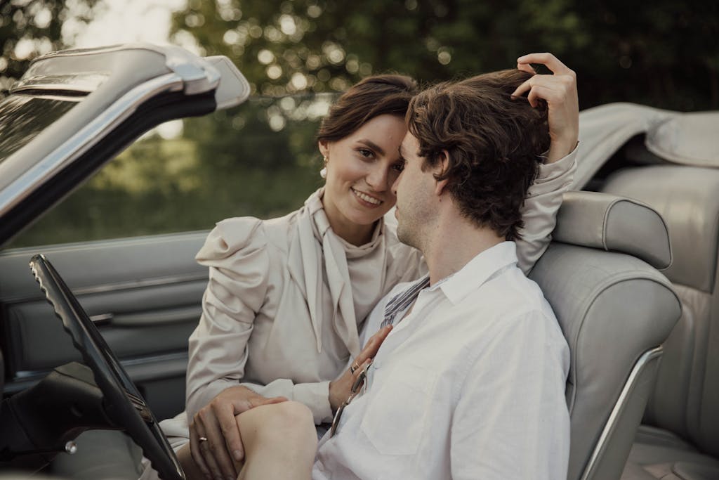 A couple enjoying a romantic moment in a convertible car surrounded by nature.