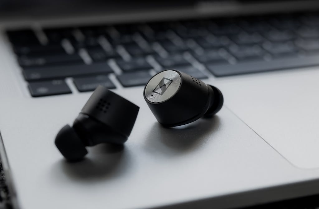 Modern black wireless earbuds resting on a silver laptop keyboard, showcasing sleek design and technology.