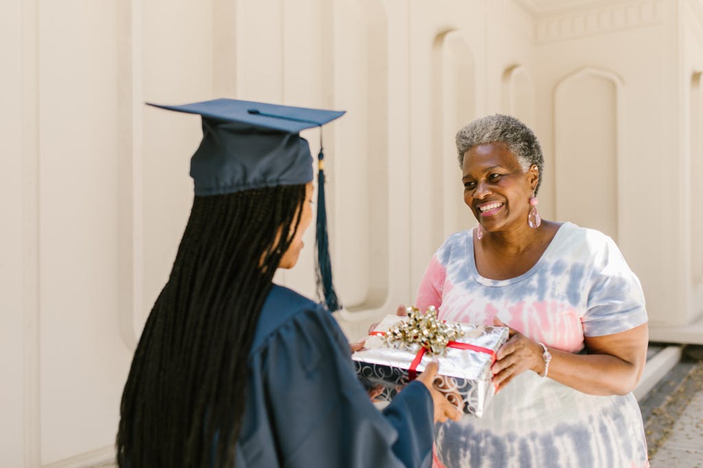 A young graduate receives a gift from a proud elder at a graduation ceremony.