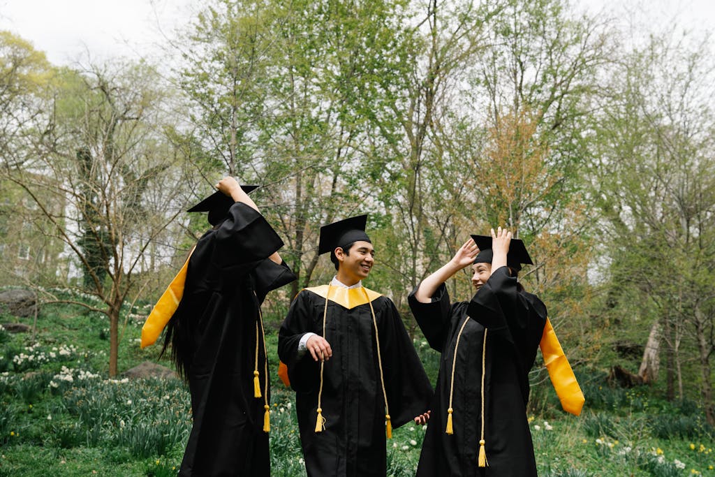 Three students in gowns and mortarboards celebrating graduation outdoors.
