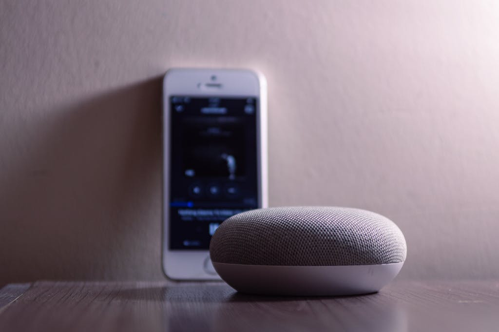 A modern smart speaker and smartphone on a wooden table, indoors.